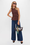 Person models the Brown Faux Suede Franz Top with stylish gold-buttoned flap pockets, paired with wide-leg jeans and chic accessories for an effortless, high-end look.