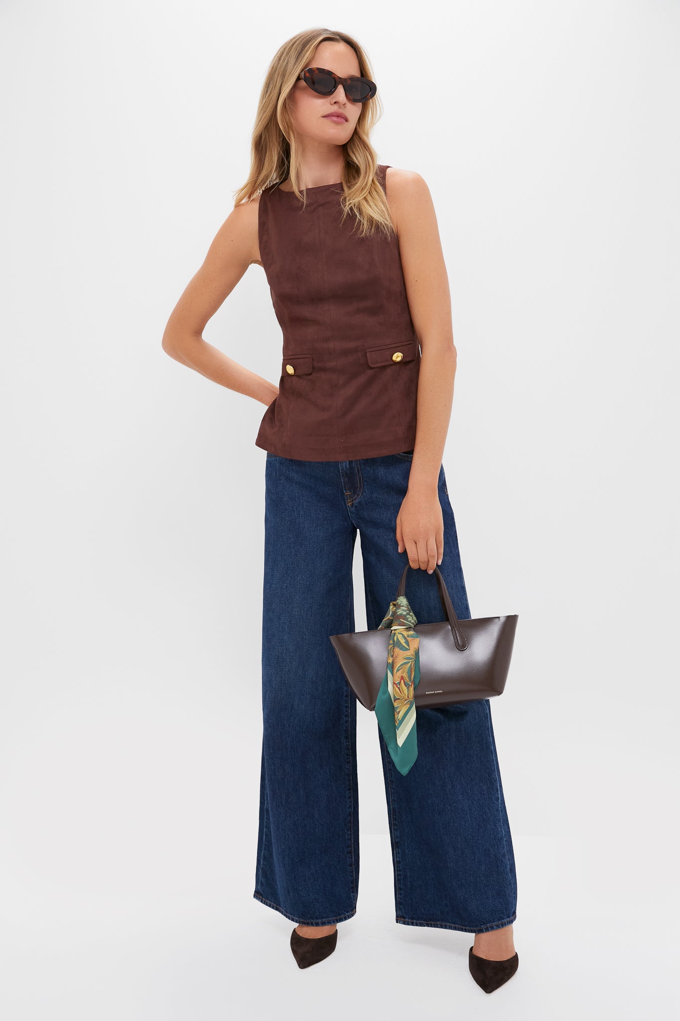 Person models the Brown Faux Suede Franz Top with stylish gold-buttoned flap pockets, paired with wide-leg jeans and chic accessories for an effortless, high-end look.