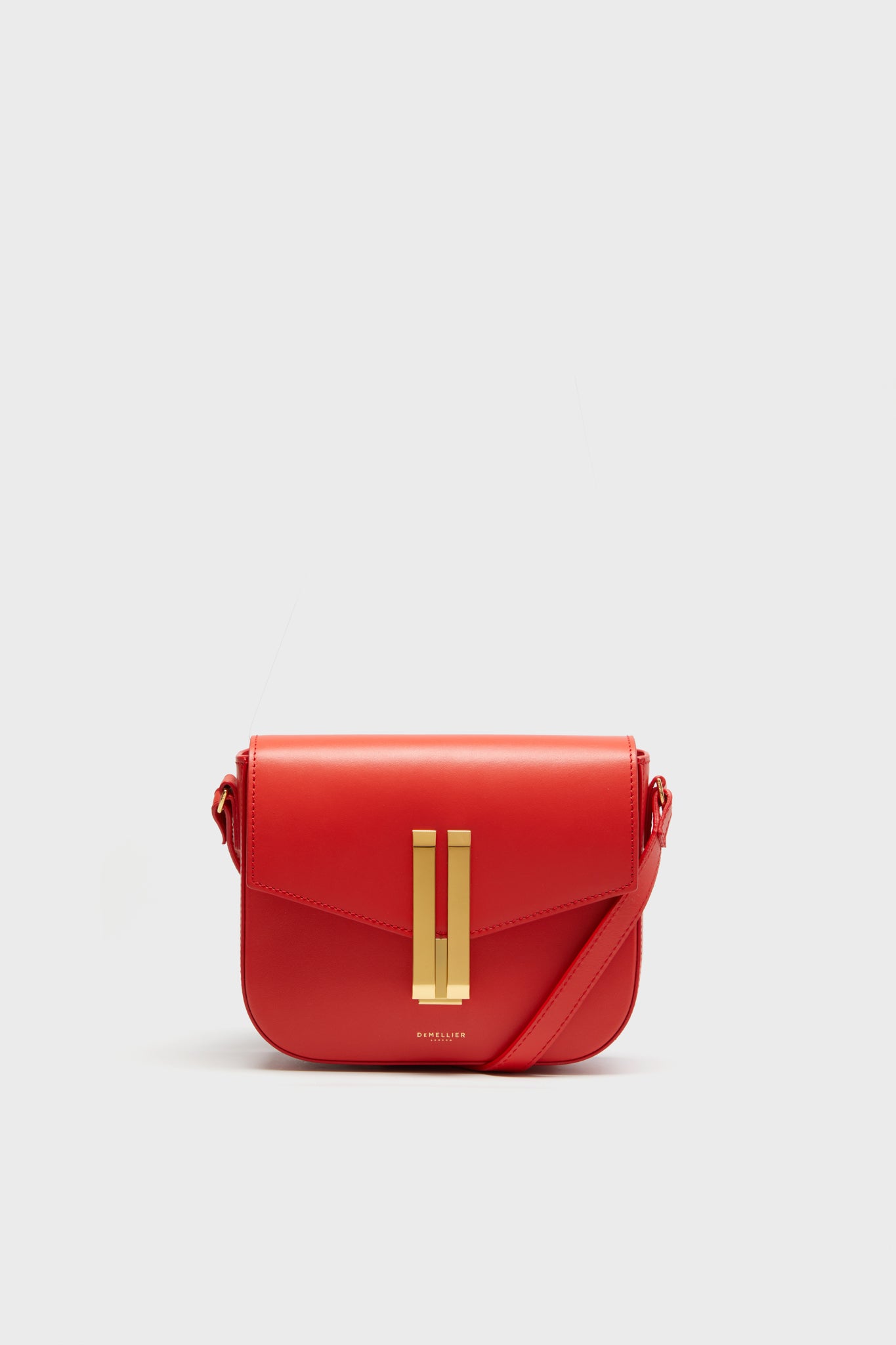 A red Italian leather crossbody bag by Demellier, featuring a gold rectangular clasp and matching accents that highlight the timeless elegance of handcrafted handbags.