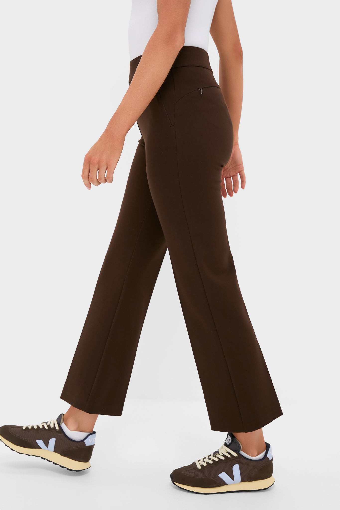 Woman in Chocolate Brown 28 Inch Compression September Pant with zip pocket detail, effortlessly styled with sneakers, embodying a classic and high-end look.