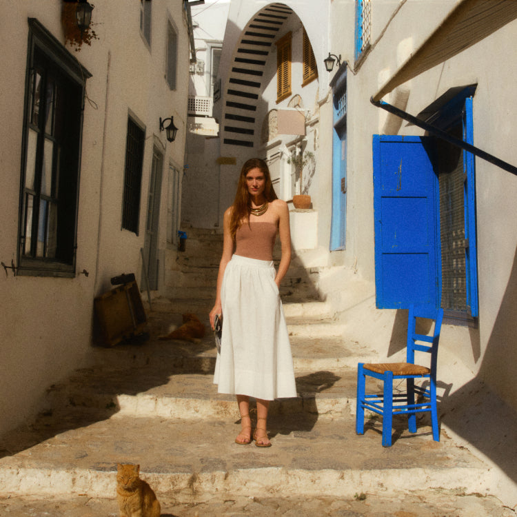 Woman standing on stairs on a street in Greece in a white skirt and truffle brown tube top. 