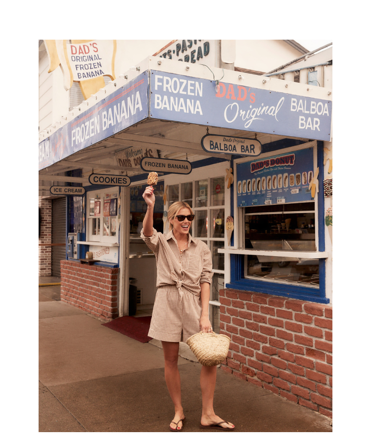 Shea McGee holding an ice cream cone above her head in brown and white gingham shorts and long sleeved button down. 