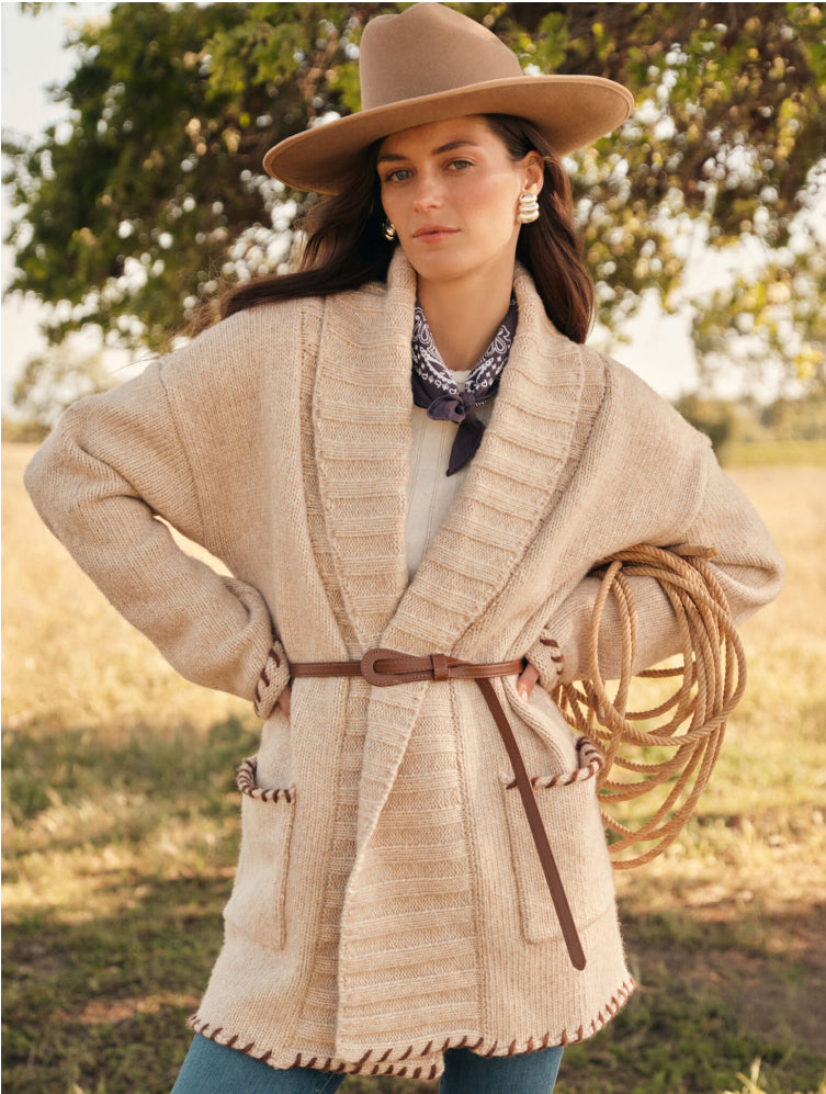 Woman in a hat, bandana, oversized sweater, and jeans. 