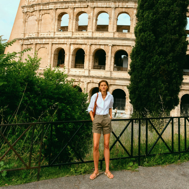 Woman standing by the Colosseum in a white shirt and olive shorts. 