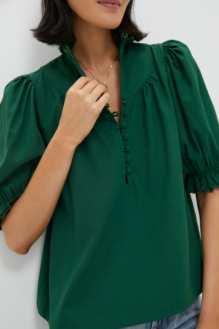 A woman in a hunter green puff sleeve top with button details and a ruffle stand collar, styled with a gold necklace.