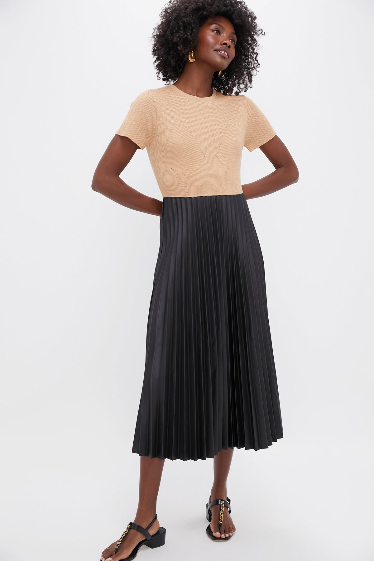 A woman wears a beige Pomander Place shirt paired with a pleated skirt.