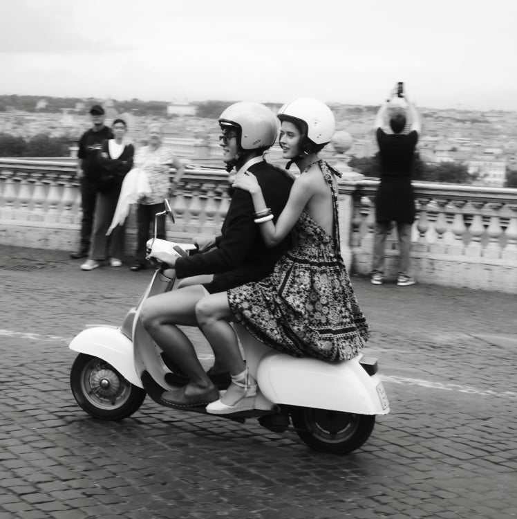 Man and woman riding a vespa through the streets of Rome. 