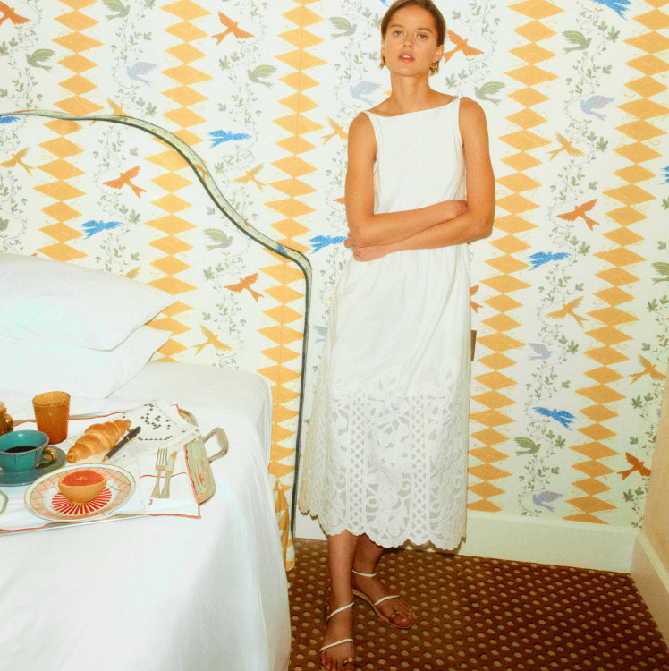 Woman standing in a bedroom with fish wallpaper in a white dress. 