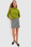 Woman wearing the Heathered Grey Marta Mini Skirt styled effortlessly with a lime-green sweater and black flats, showcasing its classic wrap button detail and high-end tailoring.