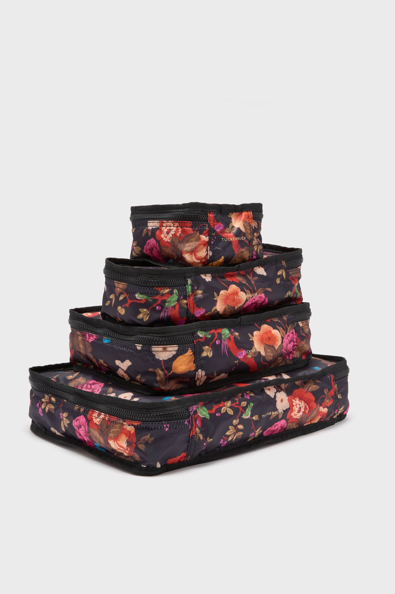 Four black Tuckernuck Accessories packing cubes, made of durable nylon with colorful floral patterns, are stacked from largest to smallest—perfect for organizing your travel essentials.