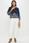 Model showcases the Navy Embroidered Lucia Blouse with elegant detailing, styled effortlessly with straight-leg white pants and tan suede accessories for a classic, high-end look.
