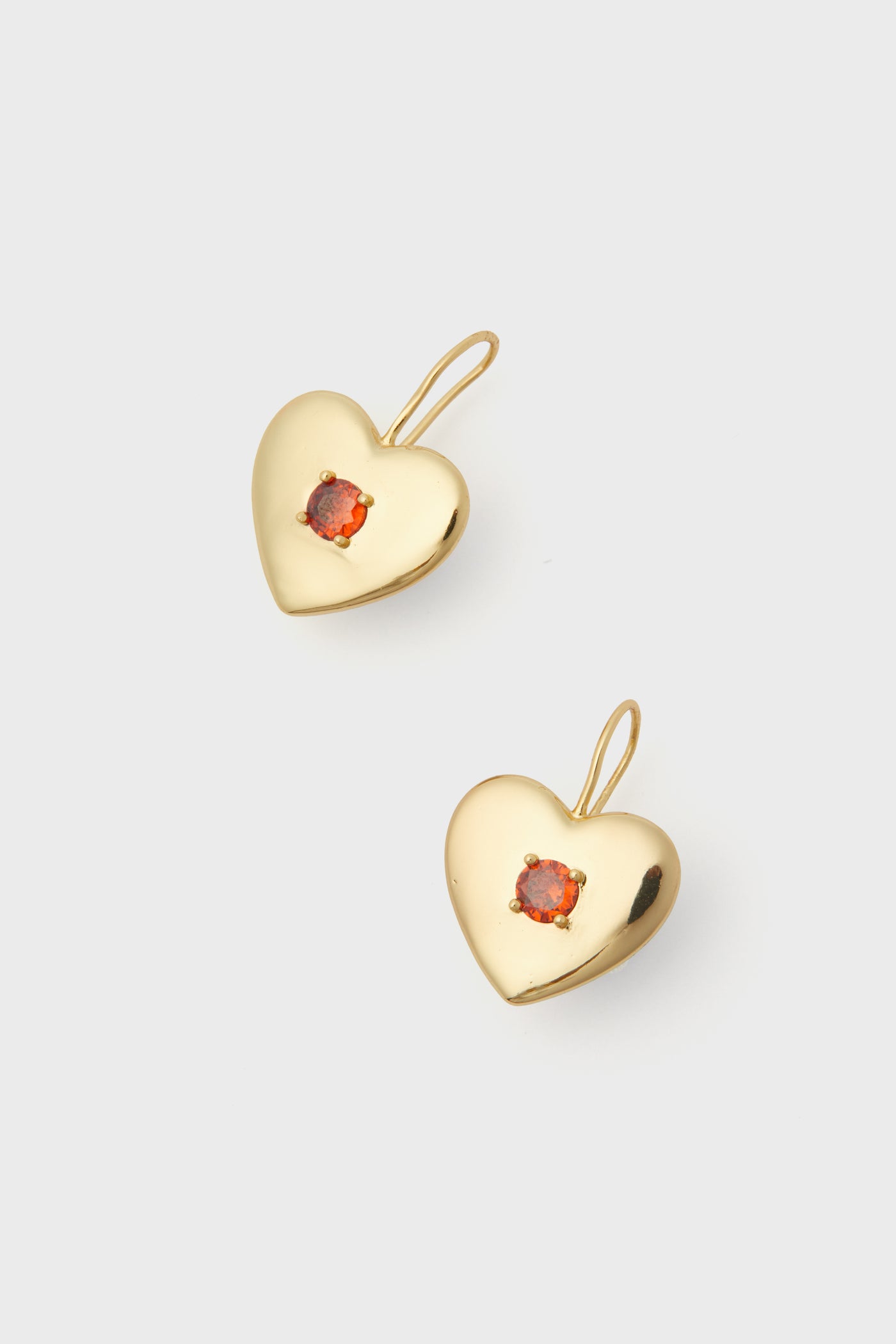 A pair of Petit Moments gold-plated heart-shaped earrings, each featuring a small orange gemstone at the center.