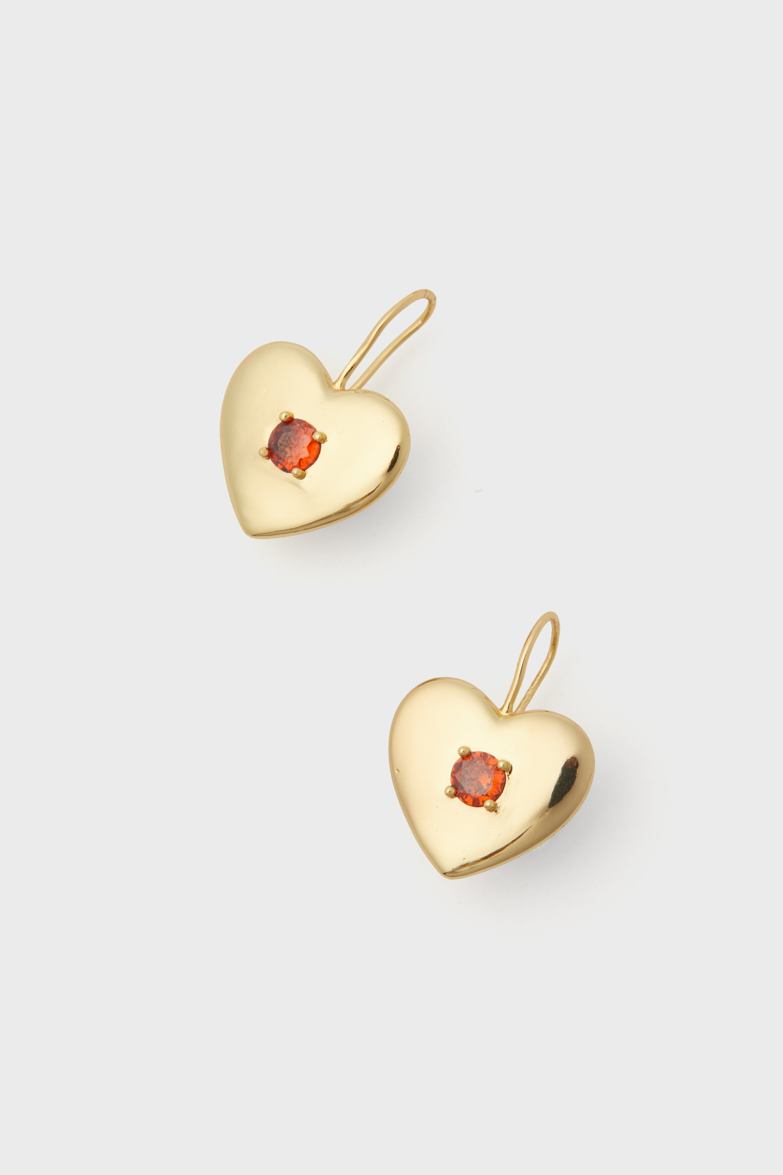 A pair of Petit Moments gold-plated heart-shaped earrings, each featuring a small orange gemstone at the center.
