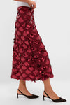 A person wearing a dazzling Hyacinth House dark red sequin midi skirt with a scalloped pattern and black pointed-toe slingback shoes.