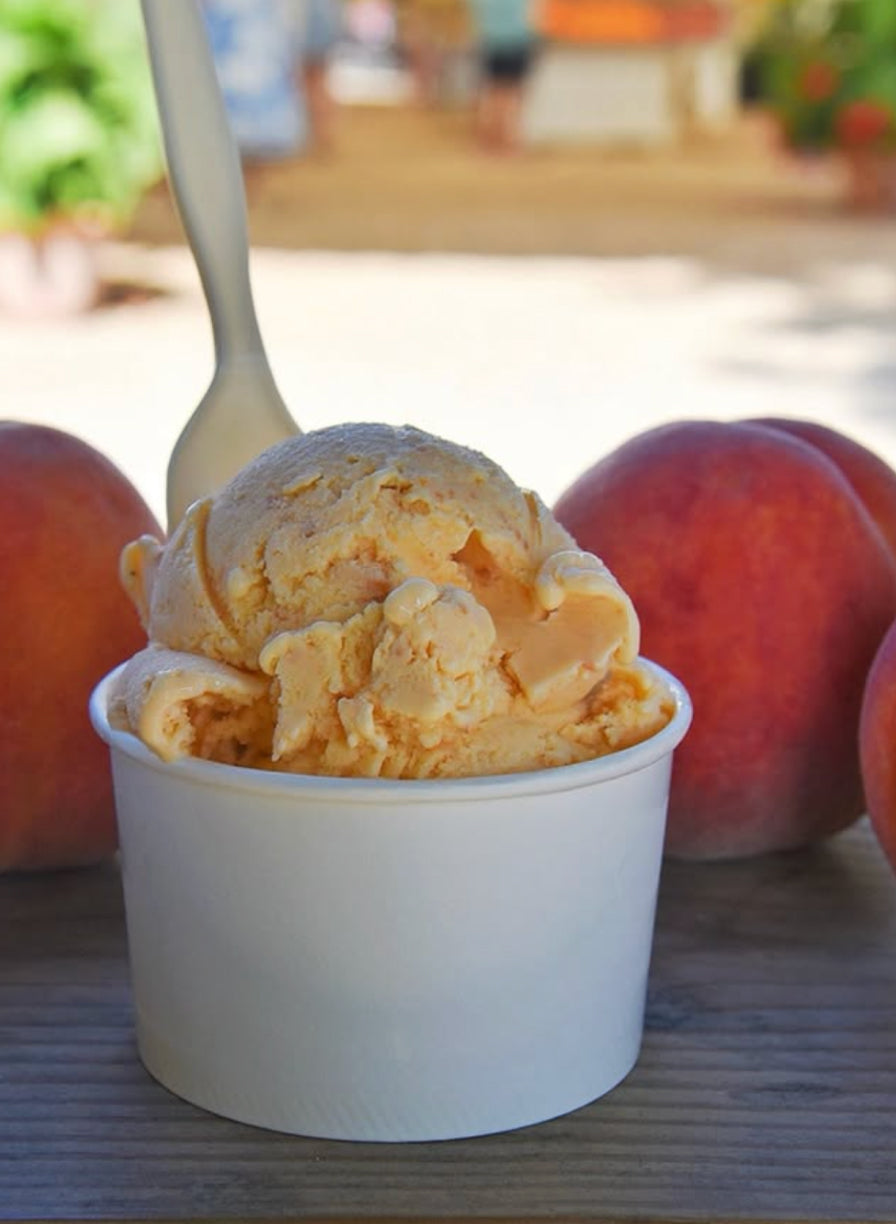 Peach ice cream in a white paper cup. 