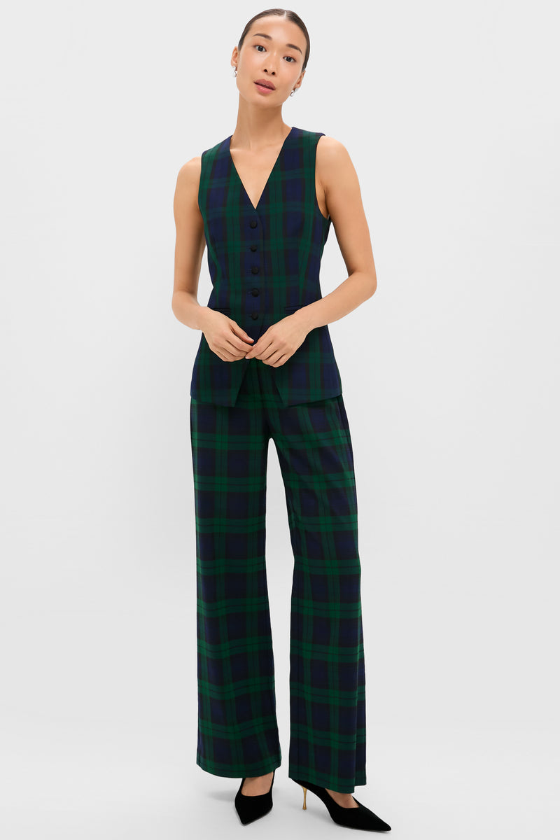 A woman stands against a white background wearing Tuckernuck's sleeveless Blackwatch Thompson Vest—a chic holiday top in dark green and navy plaid—paired with matching wide-leg pants and black heels.