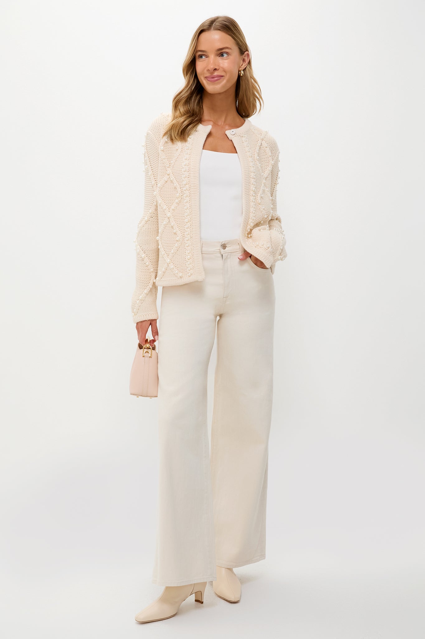 Young woman models the Cream Cable Knit Pearl Collins Cardigan, featuring a classic diamond cable pattern and pearl details, styled effortlessly with high-end, fun, winter whites.