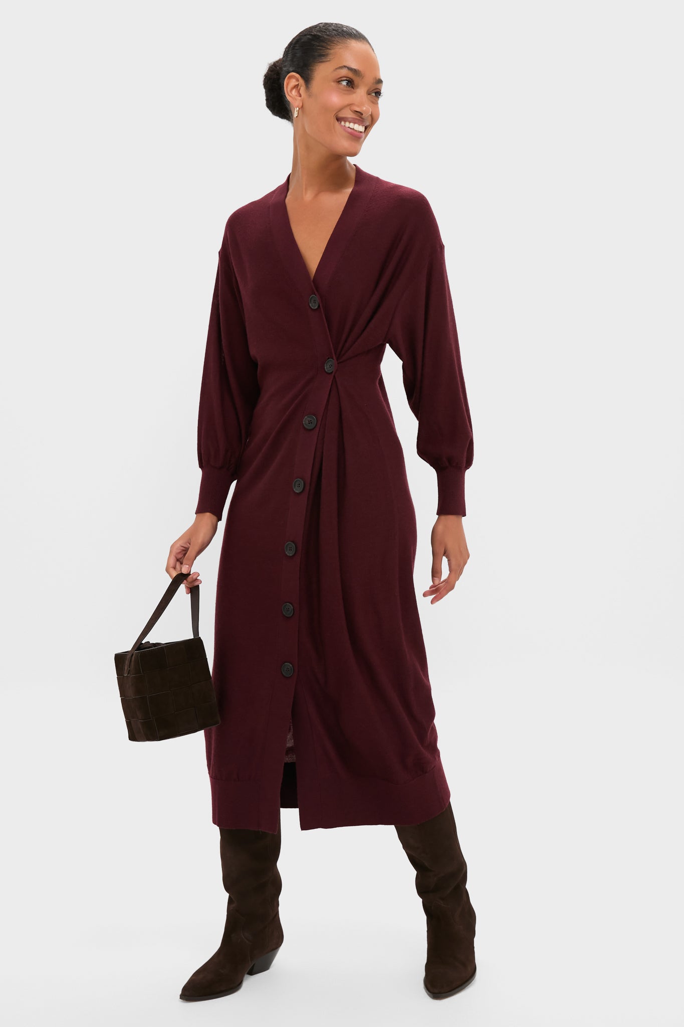 Model wearing the classic Mulberry Drippy Cardi Dress, effortlessly styled with knee-high suede boots and a woven handbag, showcasing an asymmetrical twist for a fun, high-end look.