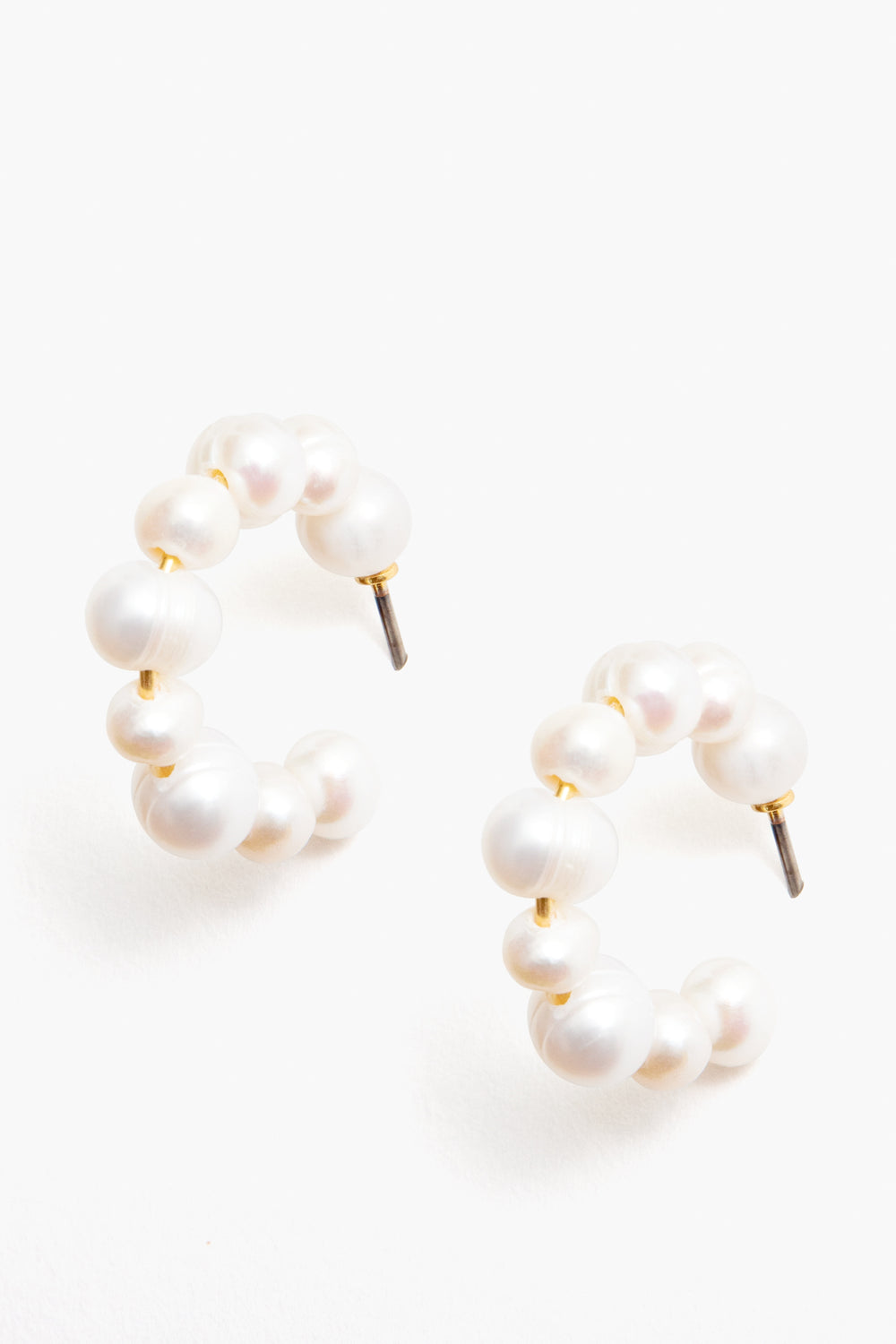 Tuckernuck Jewelry presents hypoallergenic gold hoops with round white pearls in a semi-circle design, secured with metal posts.