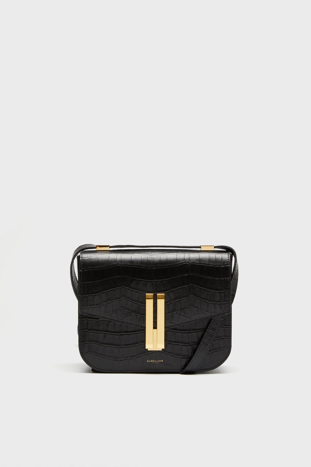 The Demellier black croc effect bag features a rectangular shape, gold-tone clasp, and adjustable crossbody strap, offering elegant style and meticulous detail.