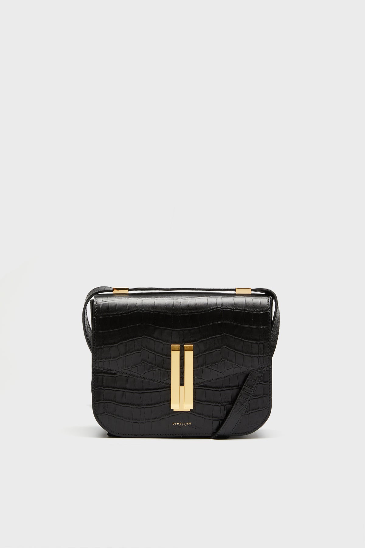 The Demellier black croc effect bag features a rectangular shape, gold-tone clasp, and adjustable crossbody strap, offering elegant style and meticulous detail.