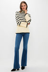 A woman stands against a white background wearing a cream and black striped sweater, Veronica Beard Beverly Skinny Flares high-waisted stretch denim jeans, and black pointed-toe shoes.