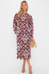 Woman in a classic, effortless burgundy midi dress with white damask print, scalloped hem; accessorized with a tan suede pouch, embodying high-end, fun style.