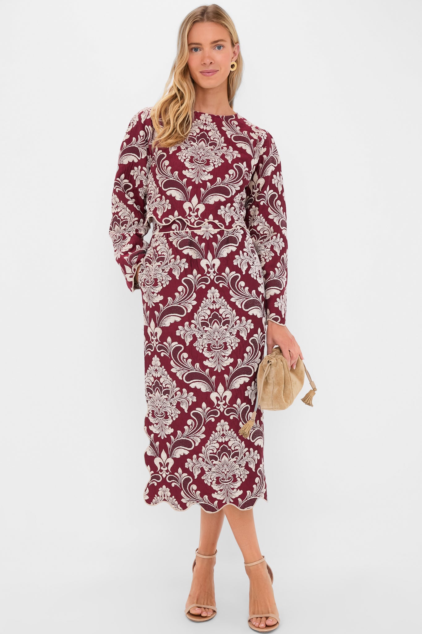 Woman in a classic, effortless burgundy midi dress with white damask print, scalloped hem; accessorized with a tan suede pouch, embodying high-end, fun style.
