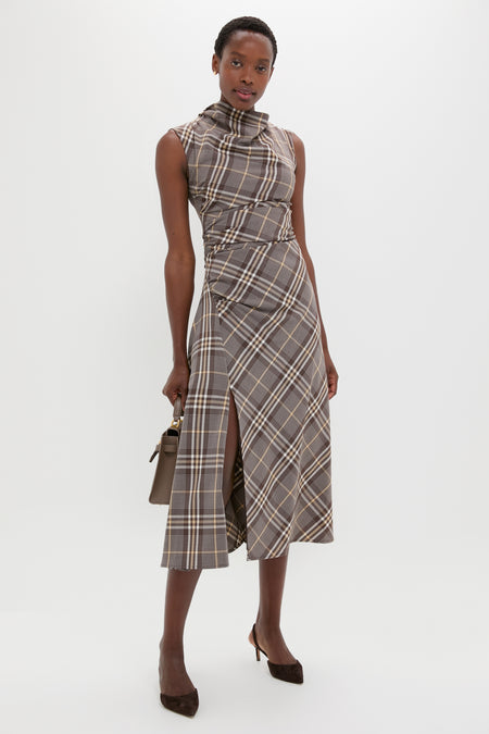 A person wears a SIMKHAI sleeveless, high-neck plaid midi dress with a front slit—ideal for occasions—styled with a brown handbag and heels, standing against a plain white background.