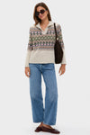 A woman in Hyacinth House sunglasses, a Fair Isle sweater, blue jeans, brown loafers, and a dark shoulder bag stands with a relaxed, stylish look.