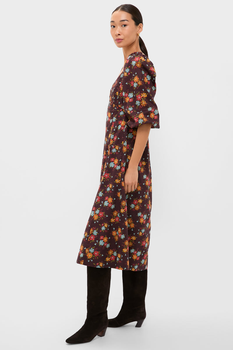 A woman stands sideways against a plain white background wearing a Love the Label autumnal floral midi dress with elbow-length puff sleeves and black knee-high boots.