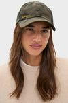 A woman wears a Barbour x Tuckernuck wax cotton camouflage cap and a beige sweater, looking at the camera with a neutral expression.
