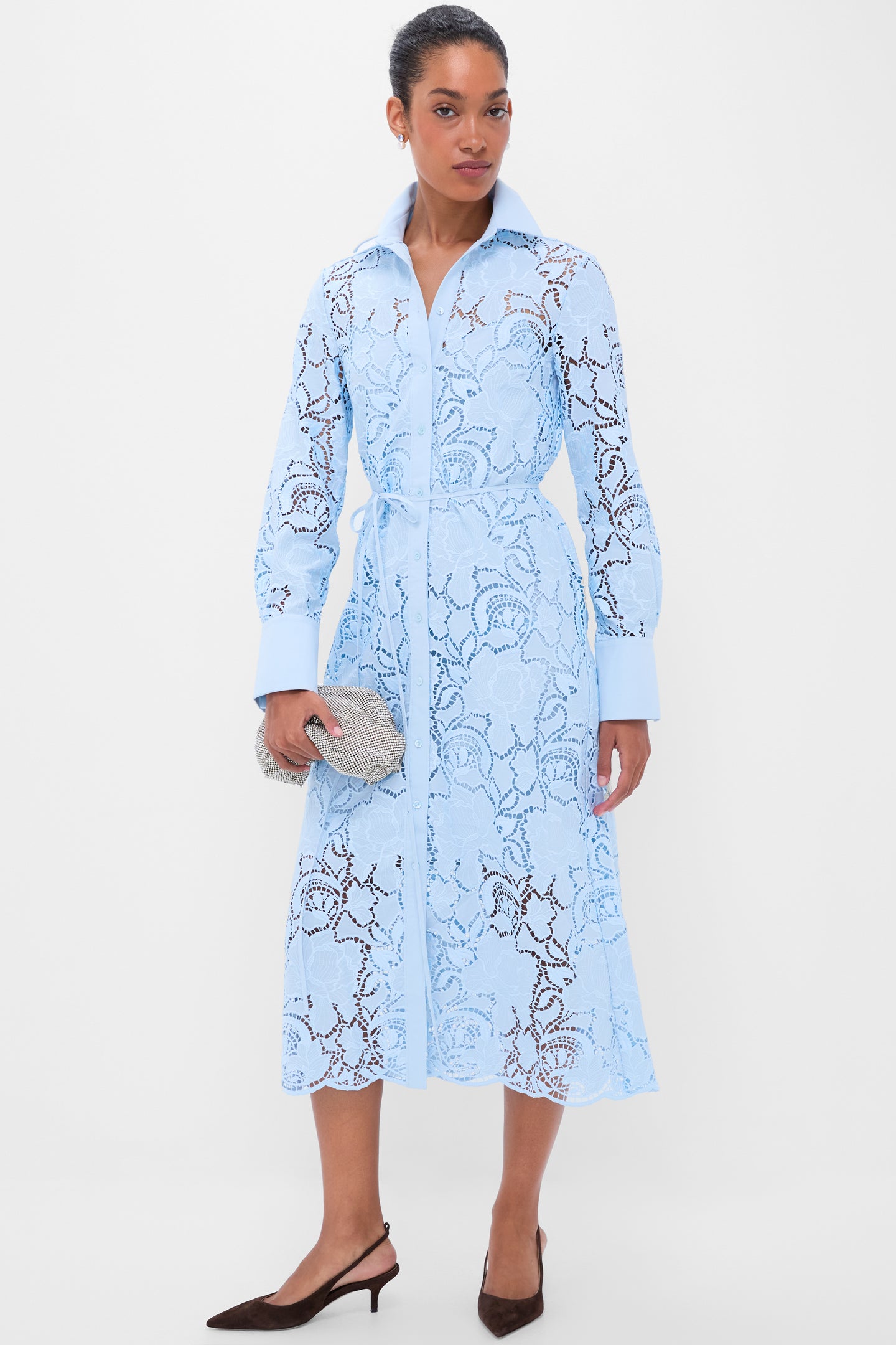 Woman models a classic, effortless elegance in a pale-blue lace shirt-dress, holding a silver clutch, embodying Tuckernuck's fun, high-end style.