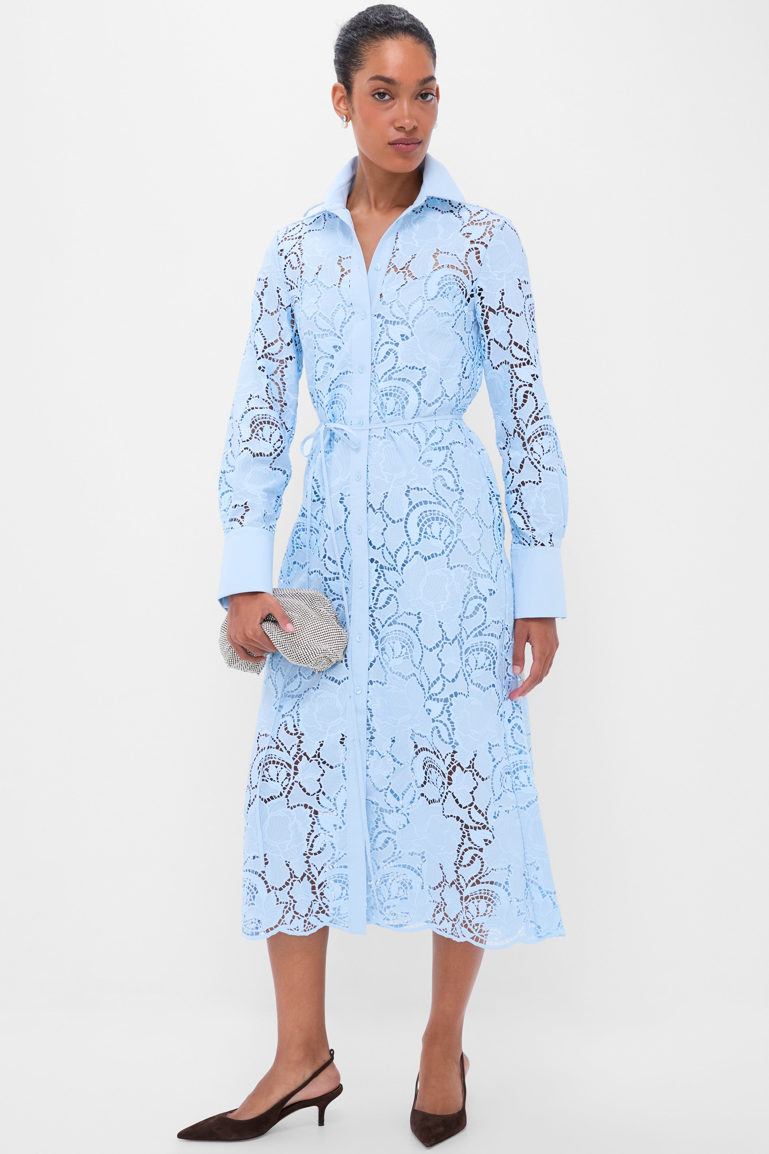Woman models a classic, effortless elegance in a pale-blue lace shirt-dress, holding a silver clutch, embodying Tuckernuck's fun, high-end style.