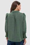Woman in Green Windowpane Seersucker Vail Blouse with puffed sleeves and smocked cuffs, styled effortlessly with jeans, embodying classic and fun high-end fashion.