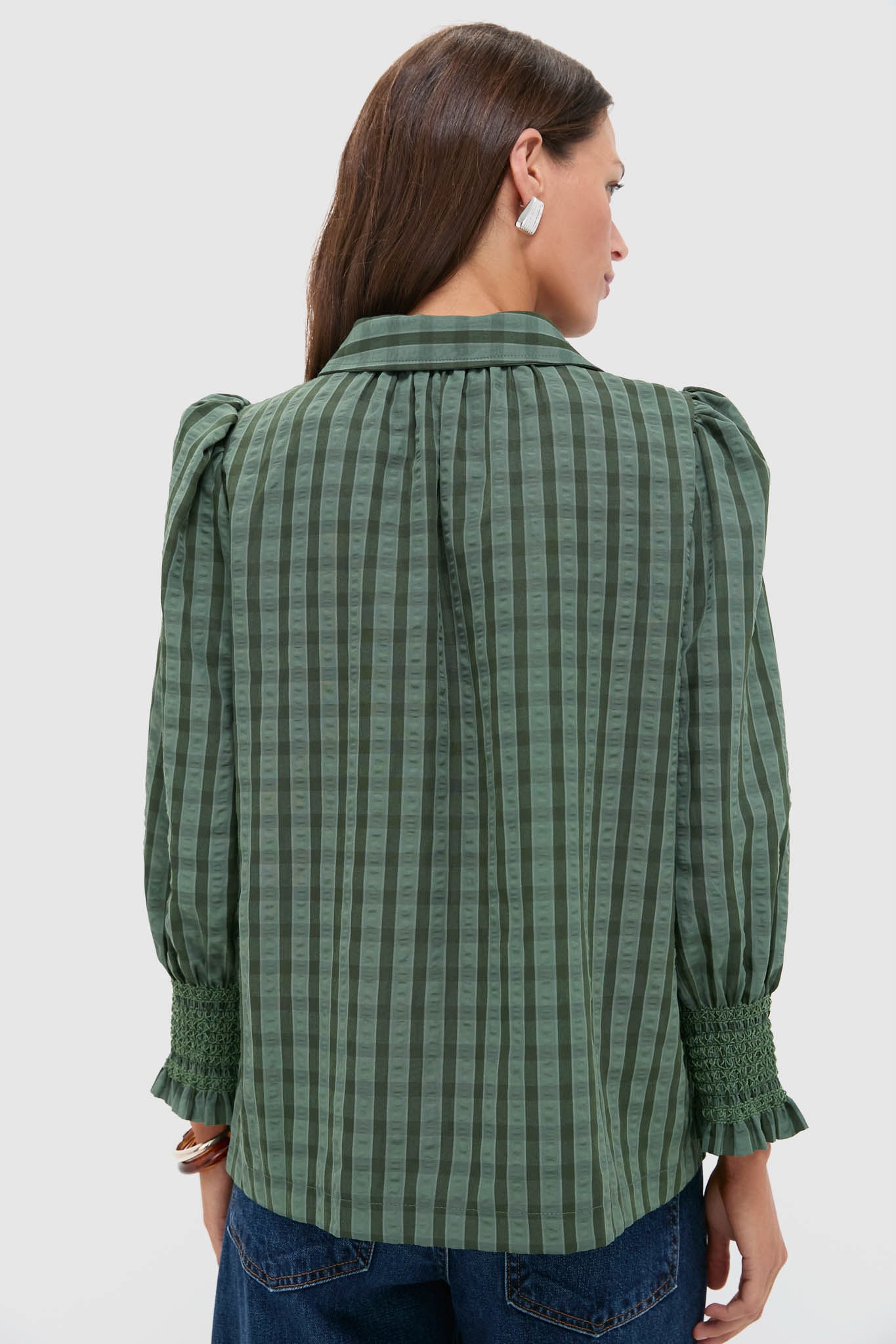 Woman in Green Windowpane Seersucker Vail Blouse with puffed sleeves and smocked cuffs, styled effortlessly with jeans, embodying classic and fun high-end fashion.