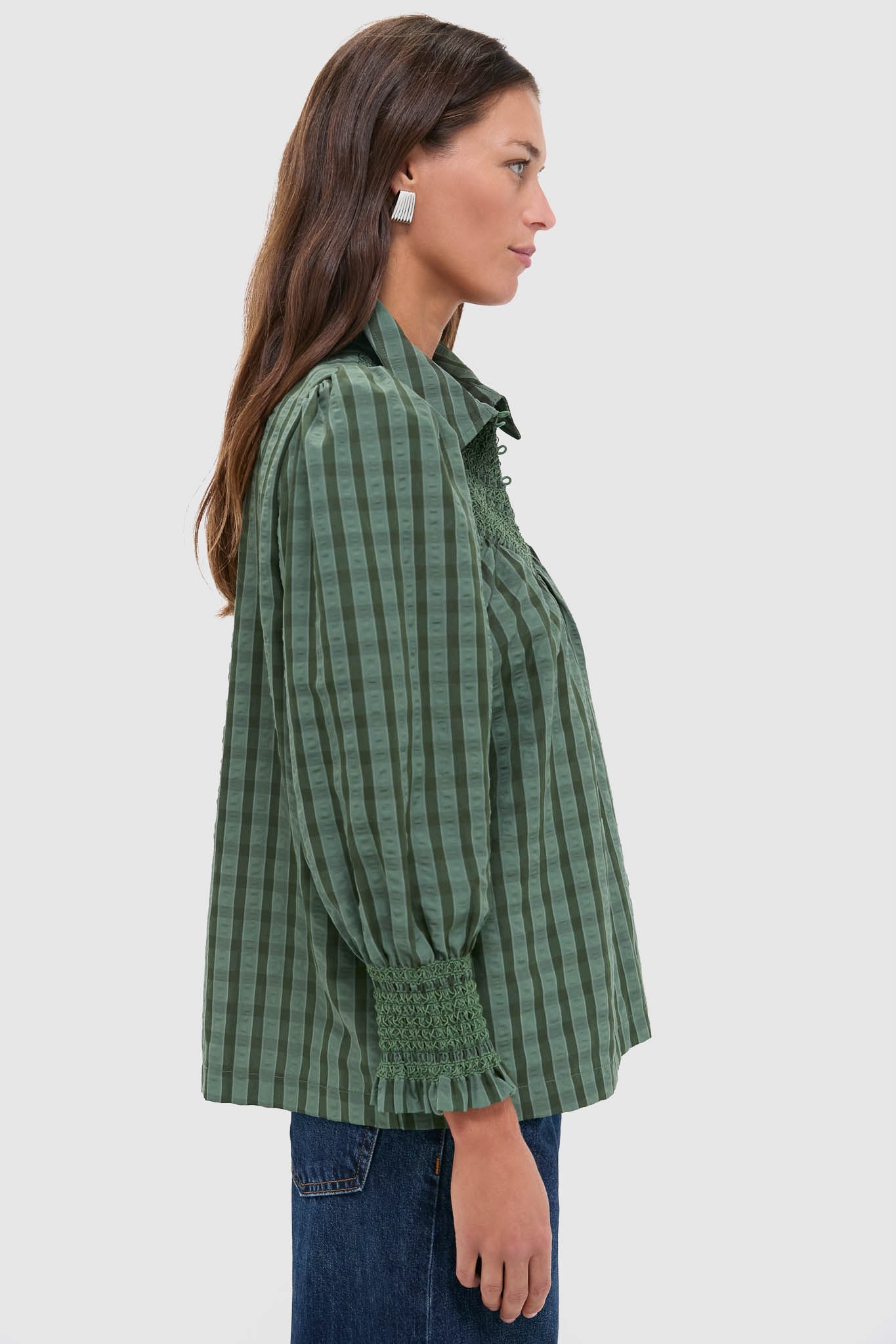 Woman models the classic Green Windowpane Seersucker Vail Blouse with puff sleeves and smocked cuffs, paired effortlessly with jeans, embodying high-end, fun style.