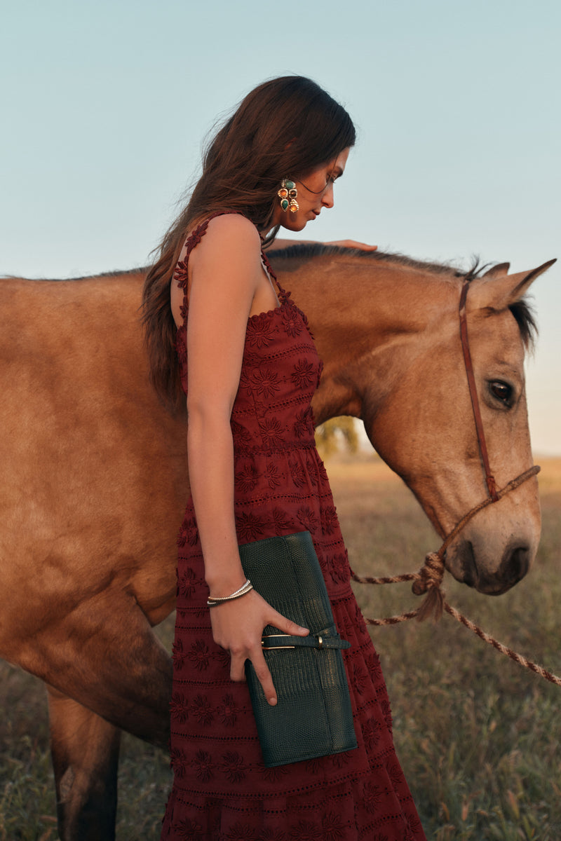 Woman in a rust colored maxi dress with eyelet details standing in front of a horse. 