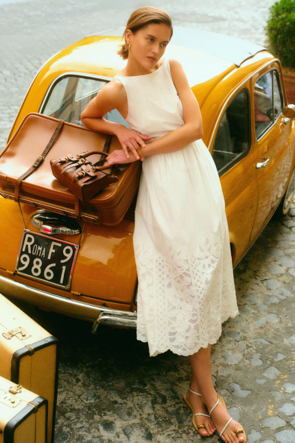 Woman leaning on a yellow car in a white dress. 