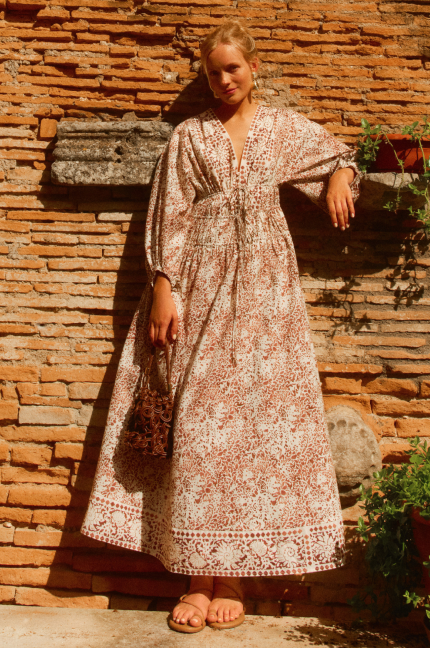 Woman standing in front of a brick wall in a long brown and white printed maxi dress. 