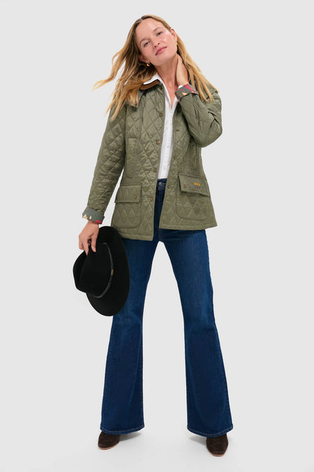 Woman in a classic green quilted jacket and jeans, holding the Black Tack Fedora Hat with leather belt detail, embodying effortless, high-end style.