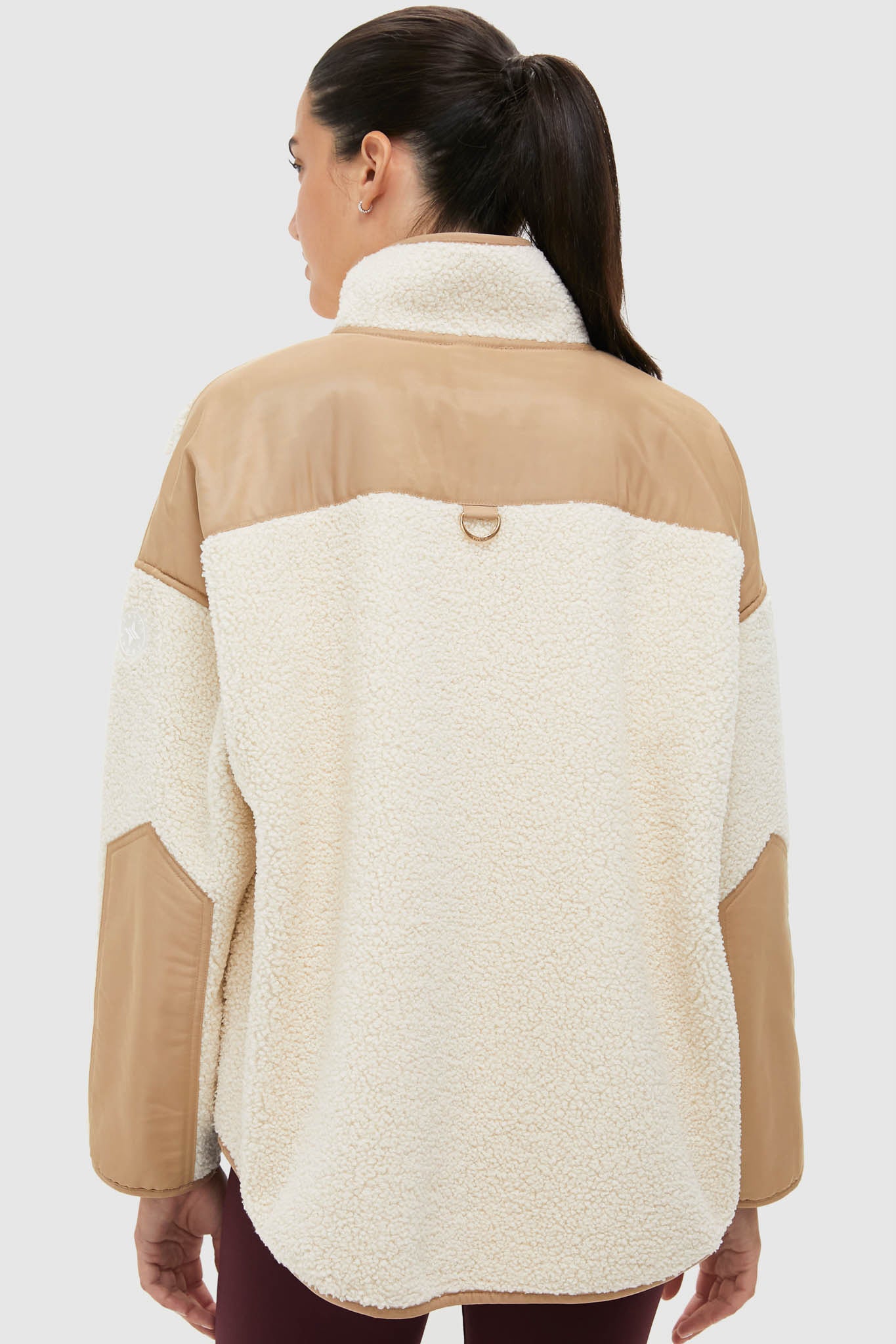 Back view of a model wearing the Buttercream Fleece Lawrence Full Length Zip Up, featuring classic sherpa texture, tan elbow patches, and effortless high-end design, ideal for fun weekend activities.