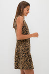 A woman stands sideways against a light background, wearing a Tuckernuck sleeveless knee-length dress in leopard print—a classic pattern that adds bold flair to this timeless silhouette.