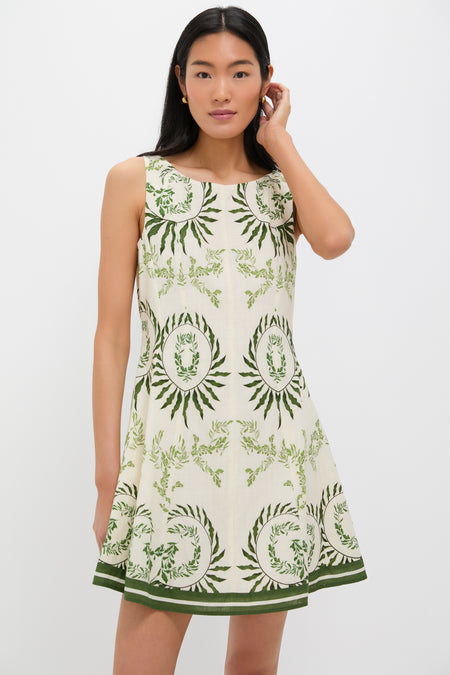 A woman wears the Anna Cate Layla Mini Dress, a sleeveless cream dress with green botanical and circular patterns, perfect for garden parties.
