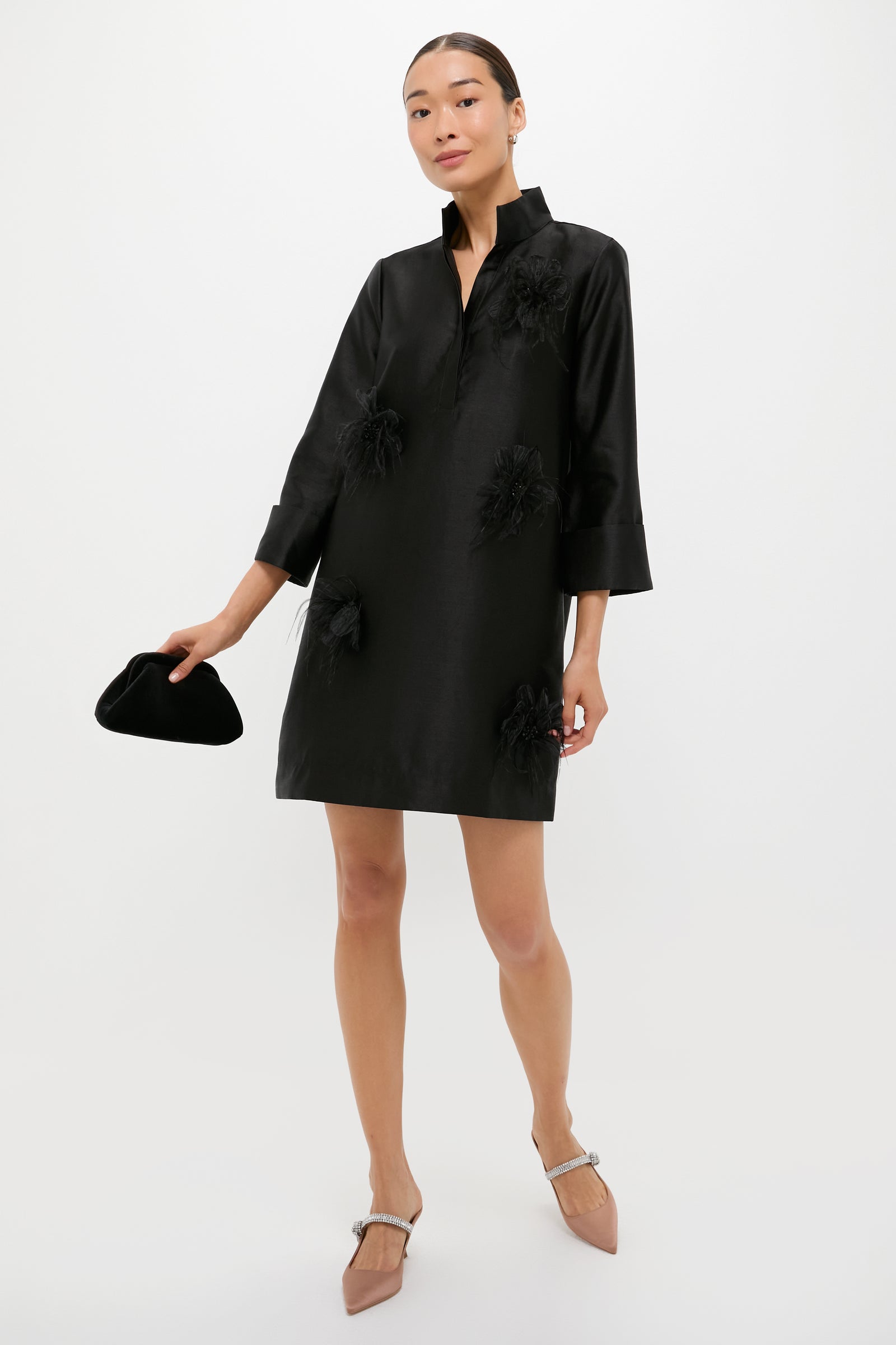 Woman models Mocha Satin Mae Heels, classic pointed-toe mules with a rhinestone strap, styled effortlessly with a loose-fit black dress and velvet clutch.