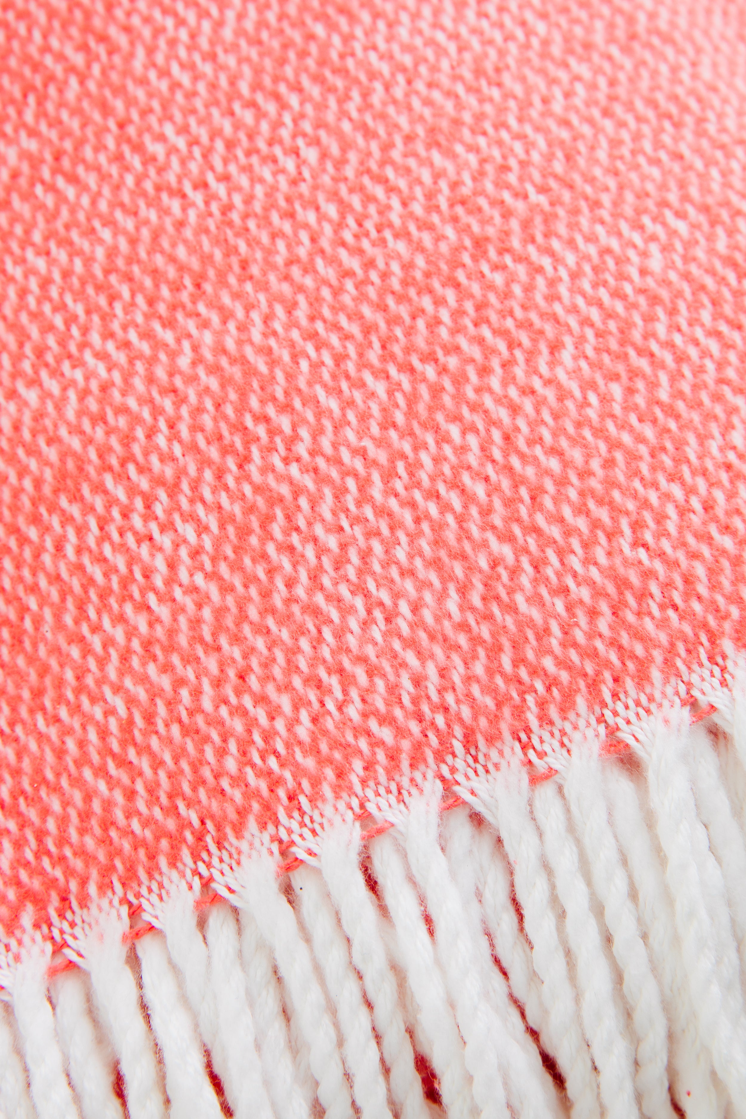 Coral Pezzo Throw with classic white fringe, effortlessly combining high-end craftsmanship and fun style in soft brushed cotton, perfect for any lounging space.