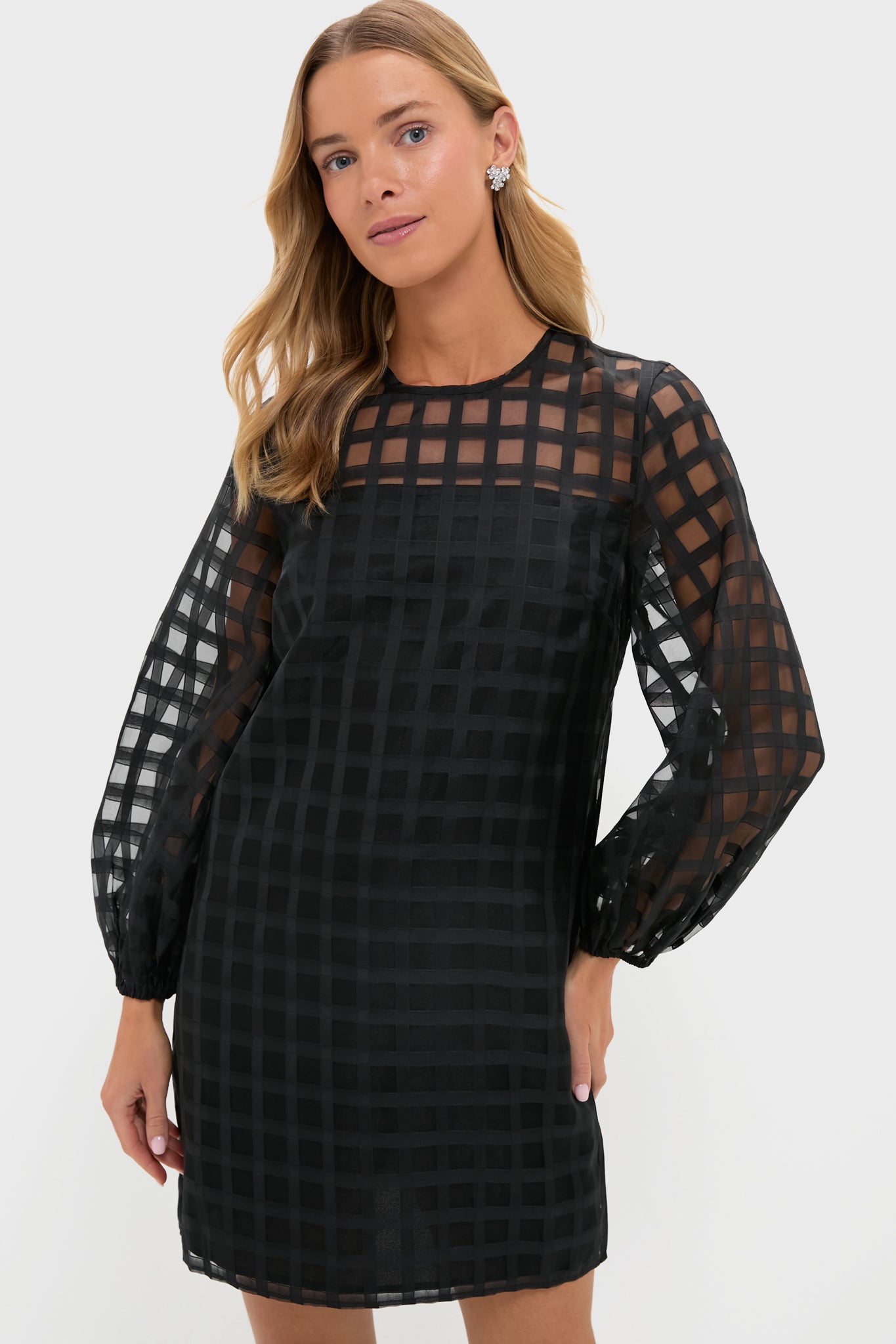 A woman wearing a Hyacinth House black long-sleeve mini dress featuring a sheer windowpane checkered grid pattern.