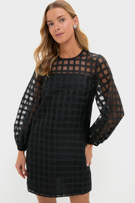 A woman wearing a Hyacinth House black long-sleeve mini dress featuring a sheer windowpane checkered grid pattern.