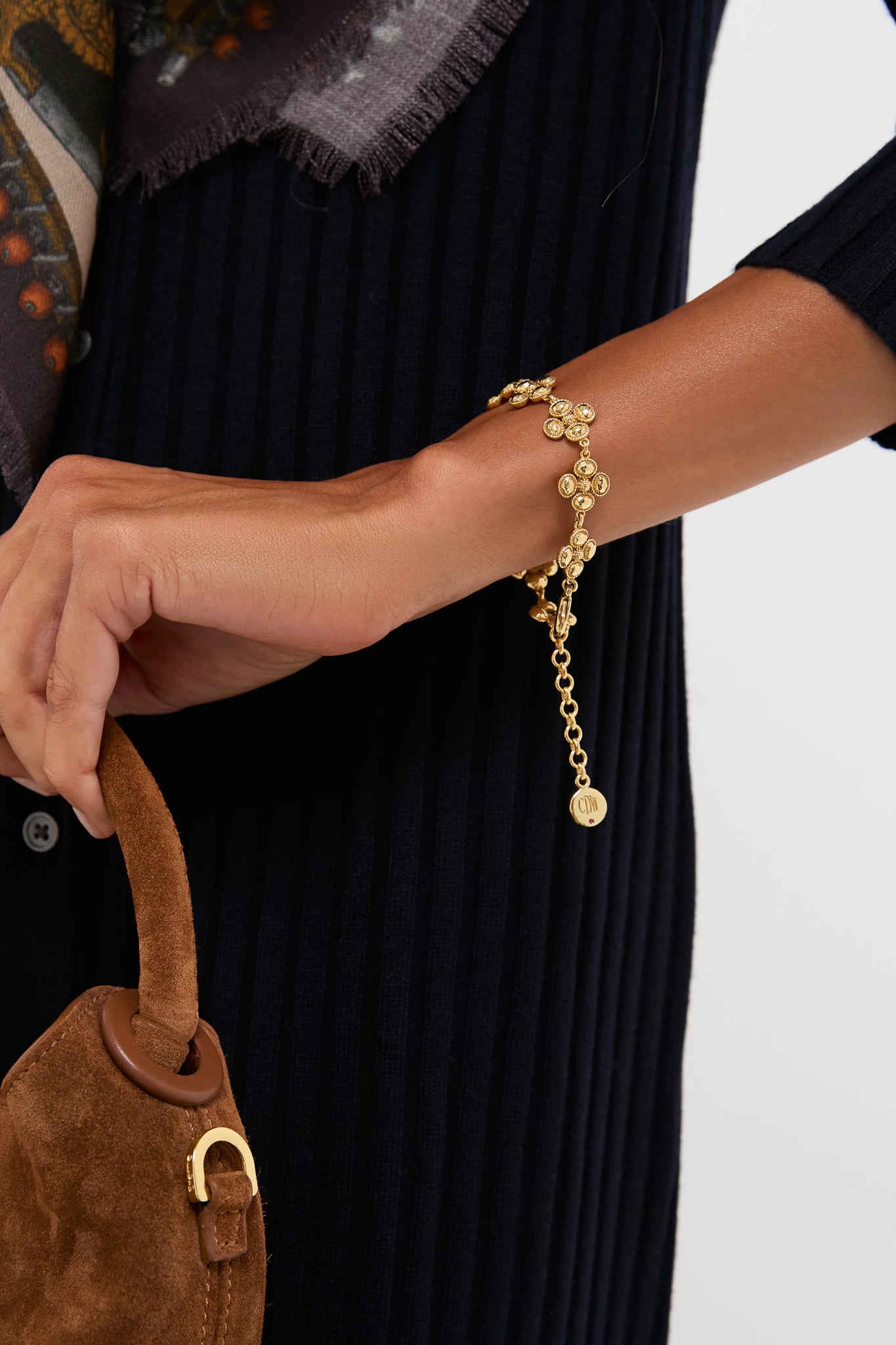 A woman’s wrist adorned with the classic Berry Clover Linear Bracelet in gold, featuring delicate coin charms, effortlessly elevates her ensemble with high-end, fun elegance.