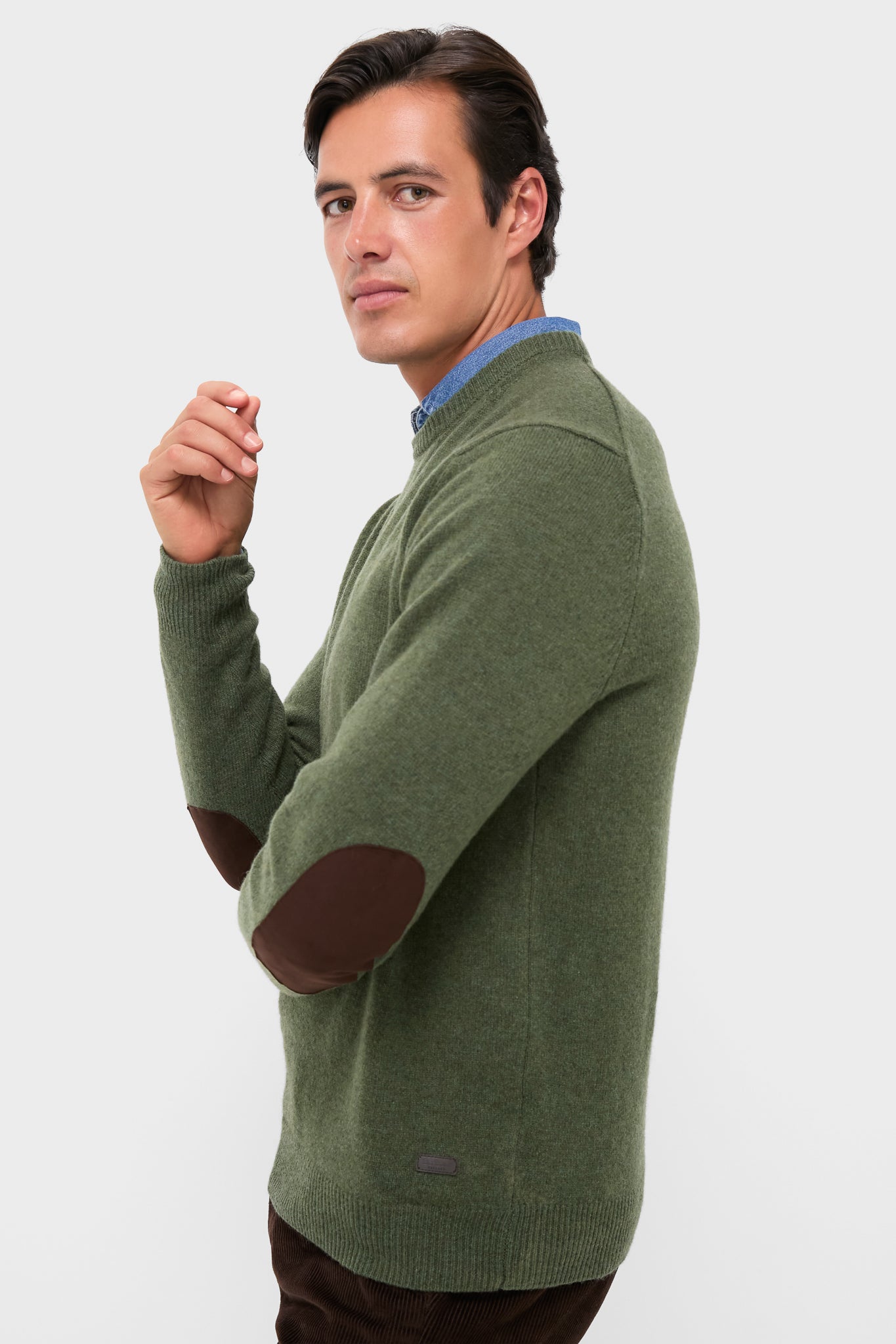 Man wearing the Olive Essential Patch Crew Neck Sweater, featuring classic leather elbow patches over a blue shirt, embodying effortless, high-end style.